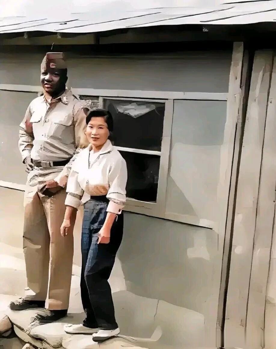 50年代，一名为美军提供特殊服务的韩国女性与黑人士兵的合影。在他们的身后的活动板