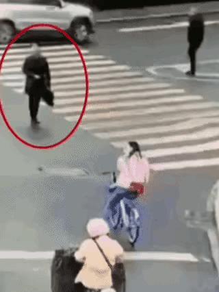 女孩骑自行车停在路边，中年男子拎着包即将过完马路时，用肩膀故意撞倒等信号的骑车女