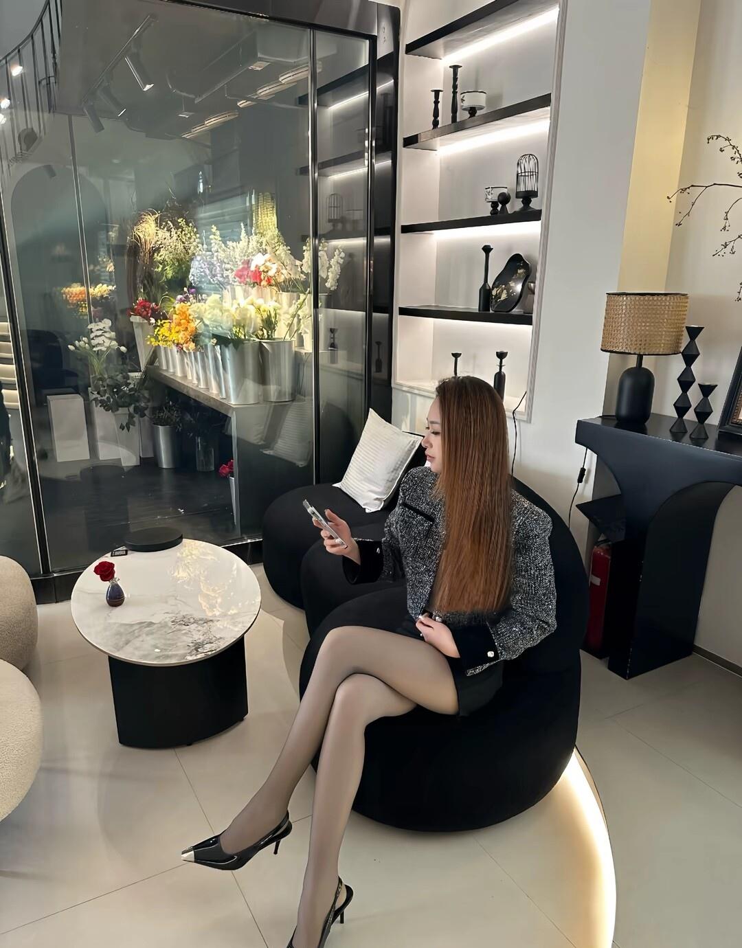优雅黑皮椅上，时尚女孩低头看手机，背景花艺装饰，尽显现代都市风。