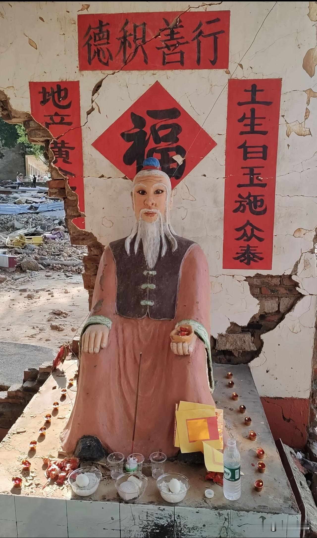 整片区域几乎全被洪水夷为废墟，唯独这尊土地公塑像连同身后的半面残墙奇迹般保留了下