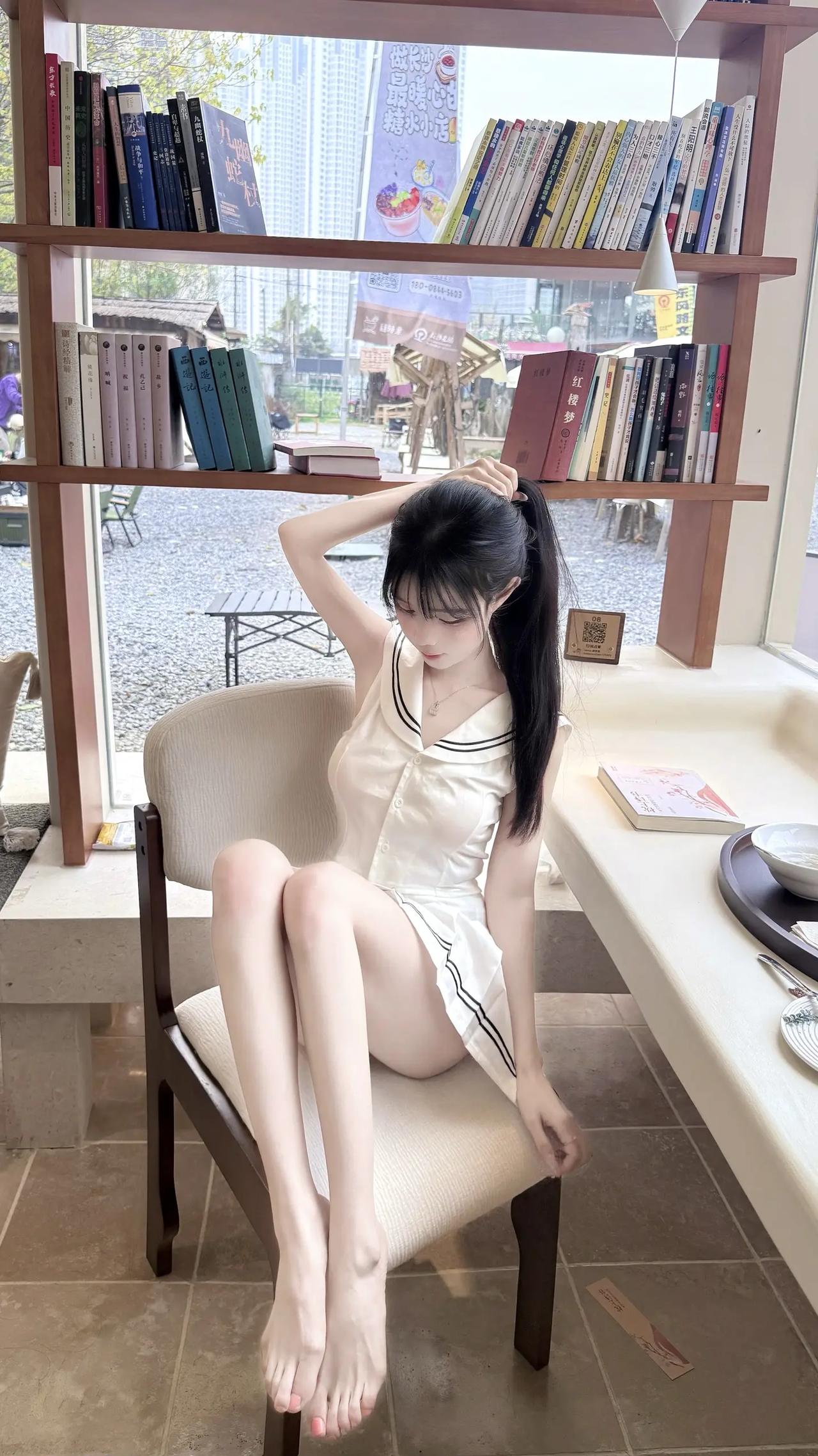 午后的惬意时光～白衣女孩在书架旁小坐，黑长发、白裙子，搭配木质书架与暖光，文艺感