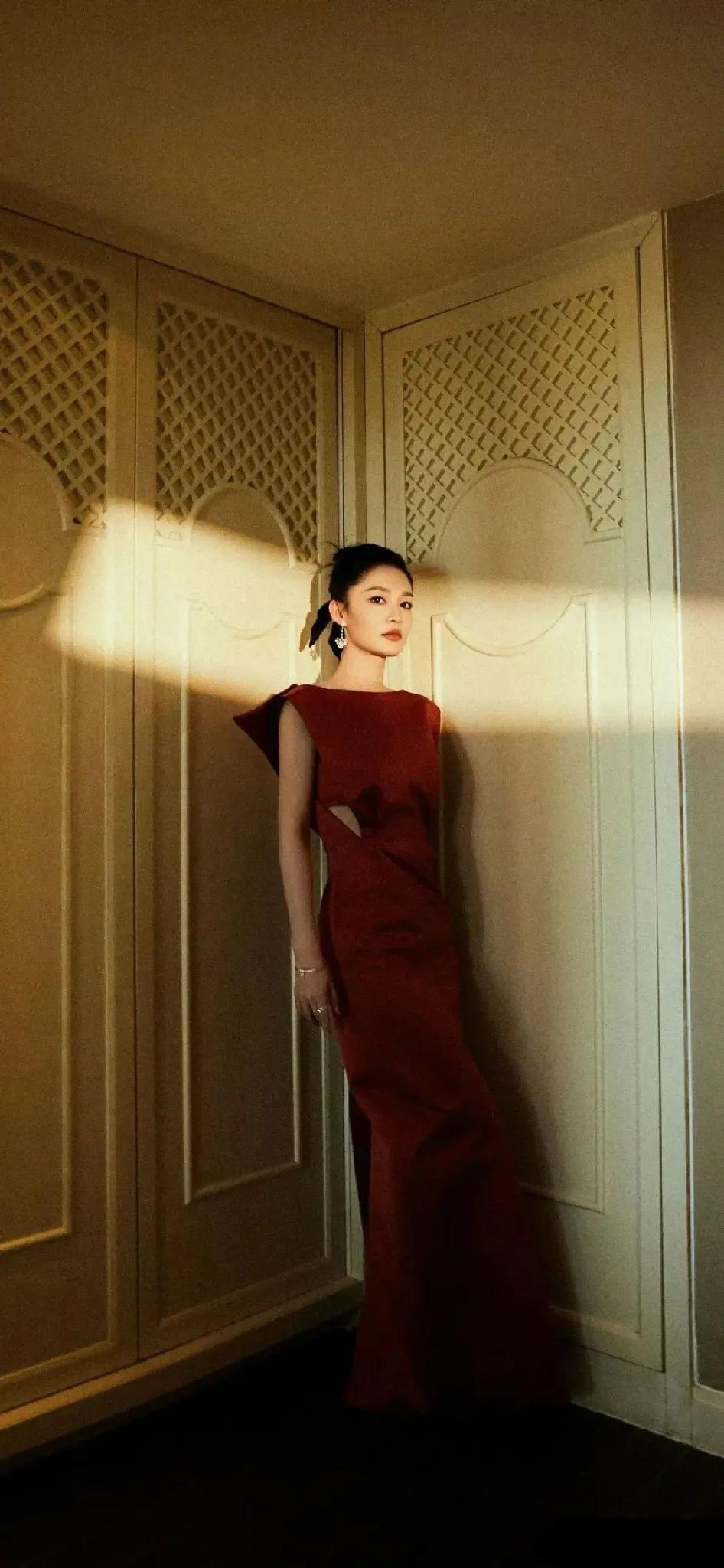 李沁身穿一袭红裙，优雅地倚靠在洁白的墙壁上，显得格外出尘脱俗。