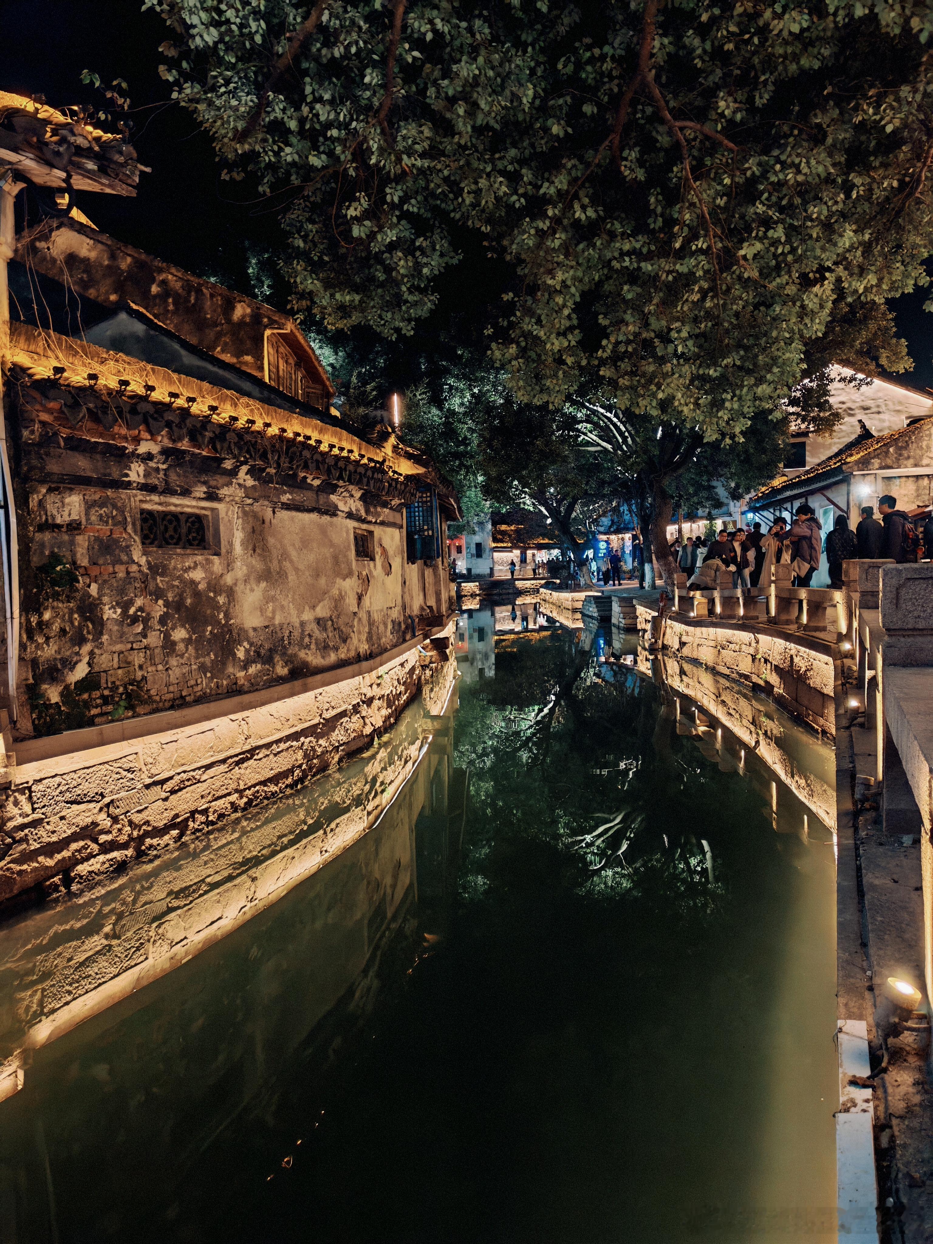 夜泊江南，灯影如梦。🌙水上集市在暮色中醒来，乌篷船载满摇曳的红灯笼，石桥下流过