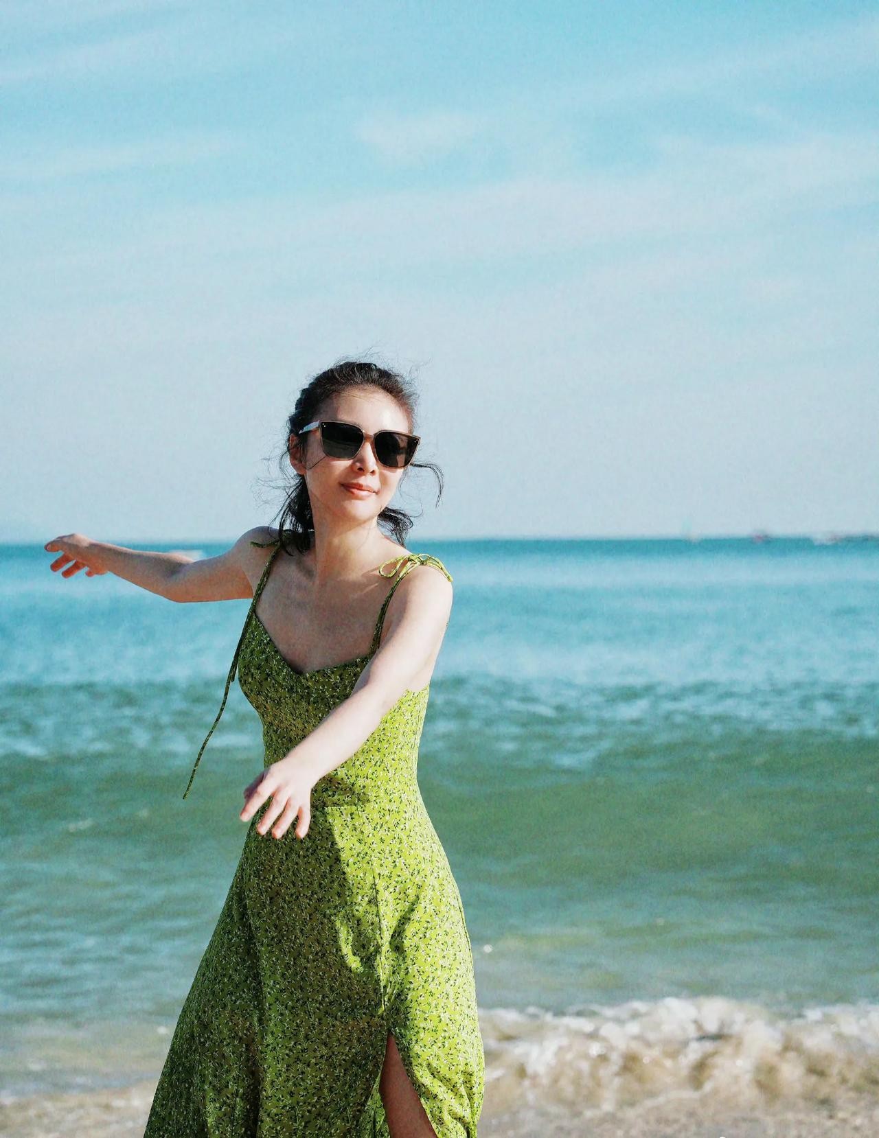 蔚蓝色的大海前面，她身穿一件浅绿色的束身长裙。戴着墨镜，阳光打在她的脸上，这样的