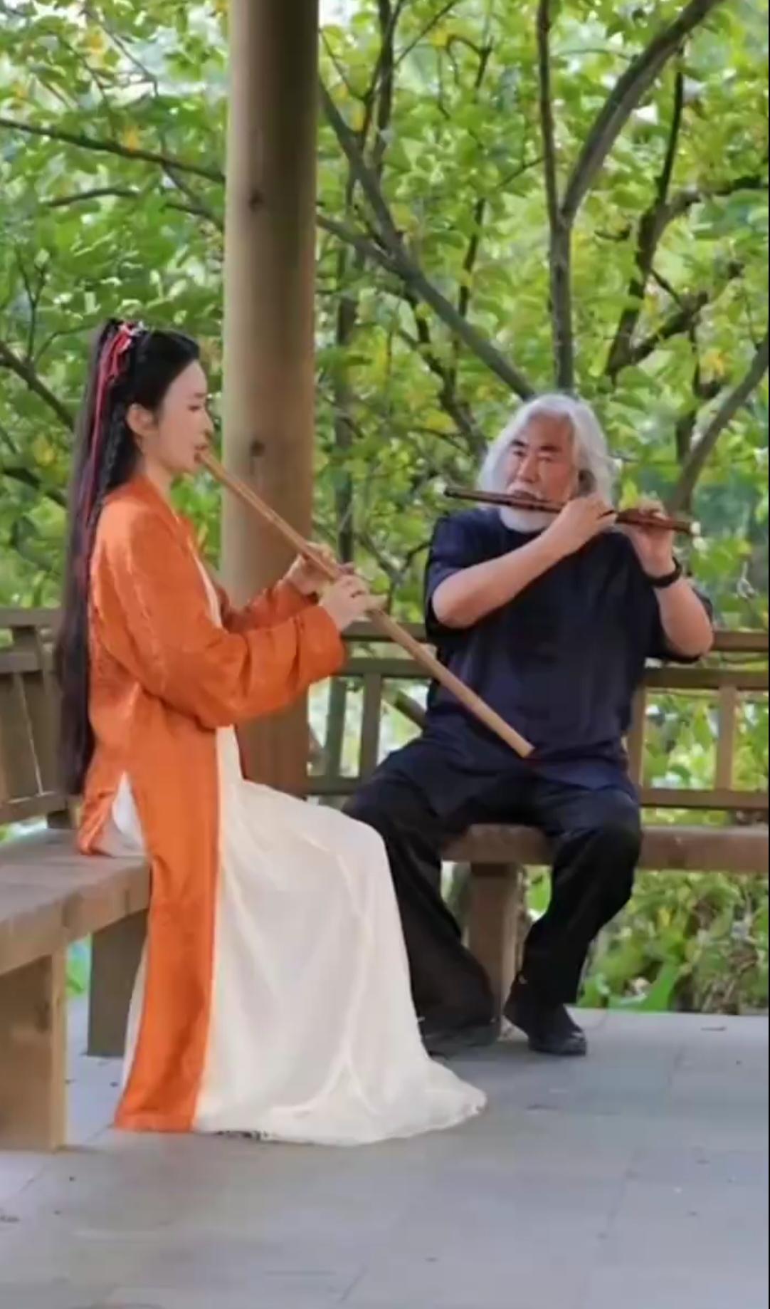 导演张纪中与妻子杜星霖琴箫想和，夫唱妇随。
杜星霖身着橙白配色的古风长裙，手持长