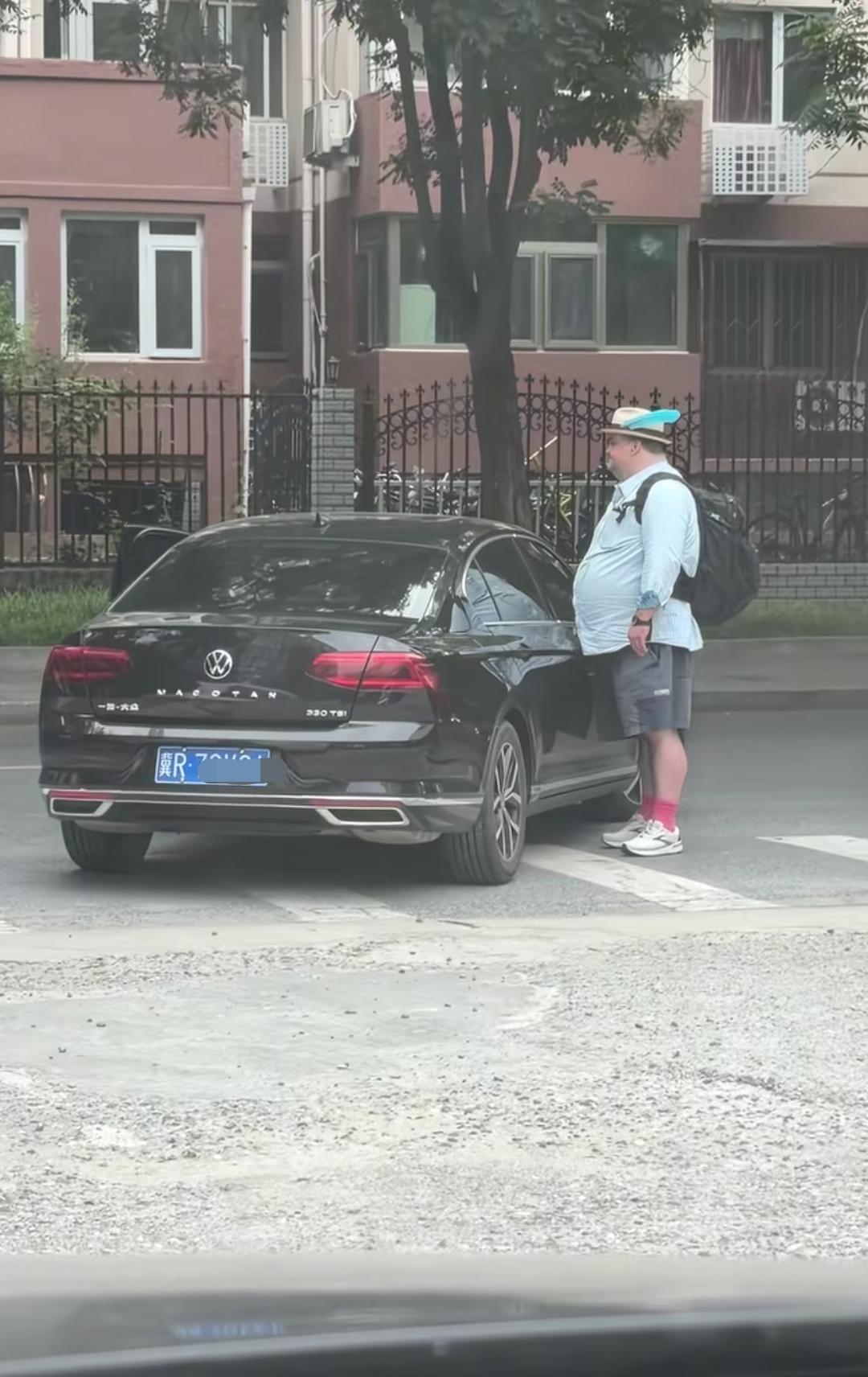 大肚子外国人走在斑马线上，一辆车要右转，外国人停下来，并没有要让黑车走的意思。僵