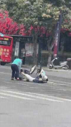 疑似广州一女士骑电动车发生事故，倒地不起，抽搐不止。一阿姨出手帮忙搬开电动车。