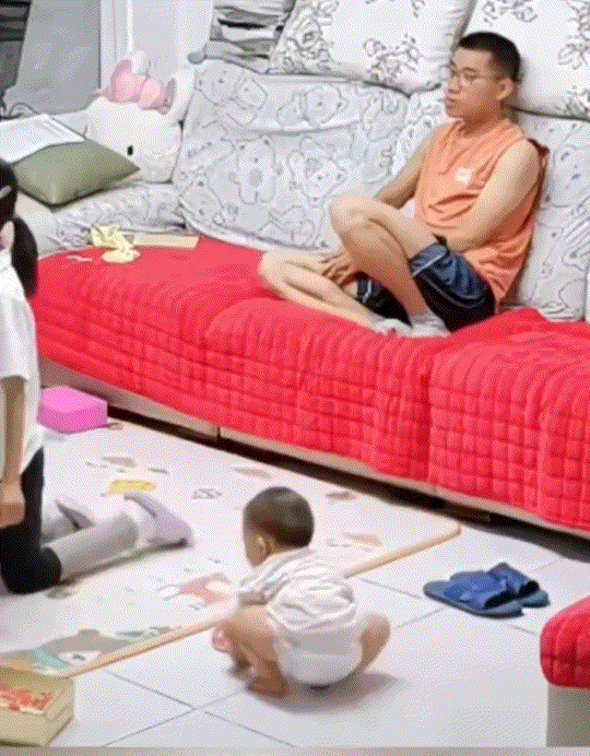 称职的好爸爸！山东，一爸爸坐在沙发上守着家中最小的娃，虽然爸爸这时还在看电视，但