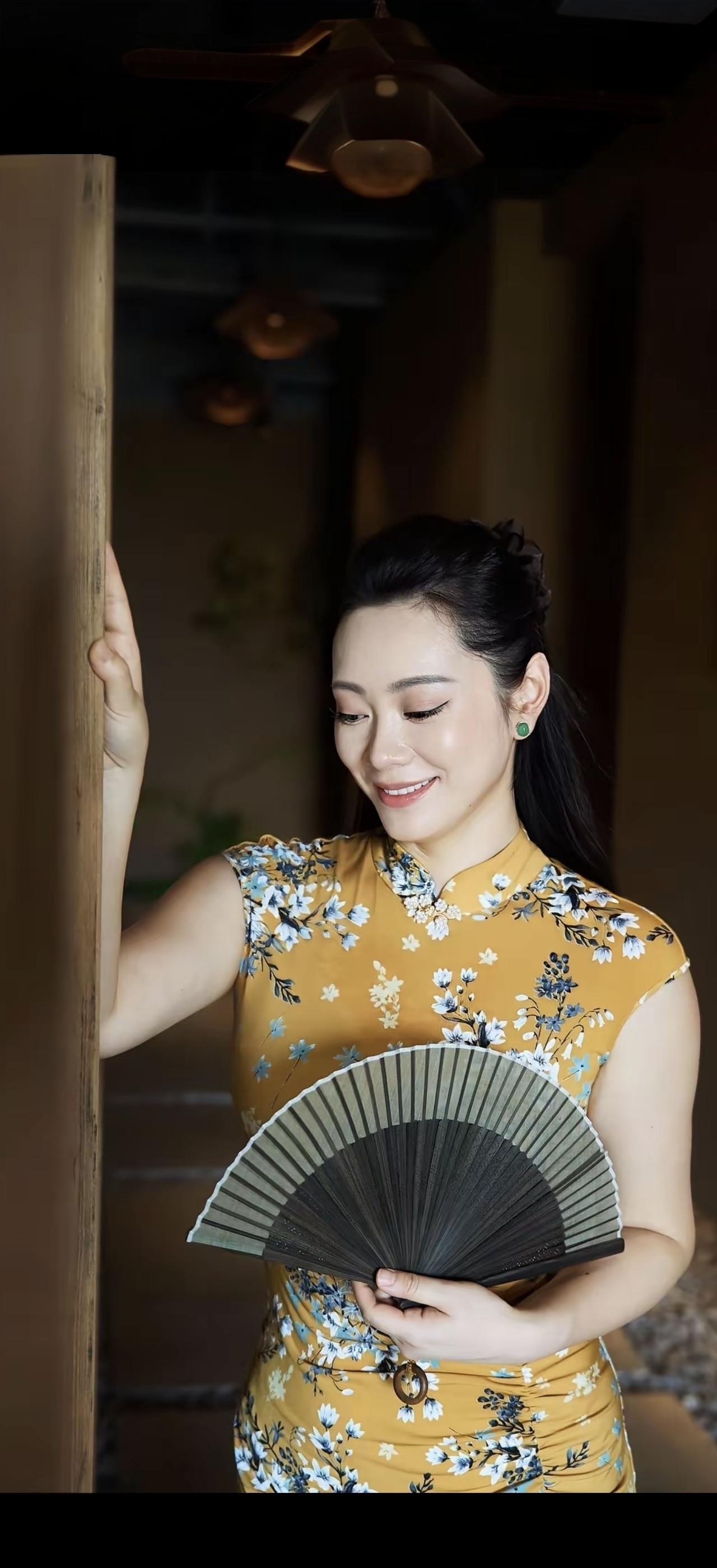 她穿着旗袍，拿着扇子，微笑着。