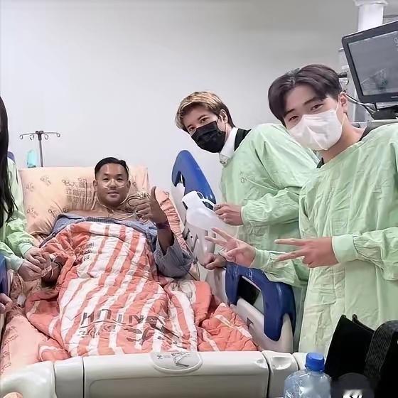 王力宏手里拿着一个尿壶，站在陈建州的病床边。照片是陈建州自己今天发的。他穿着条纹