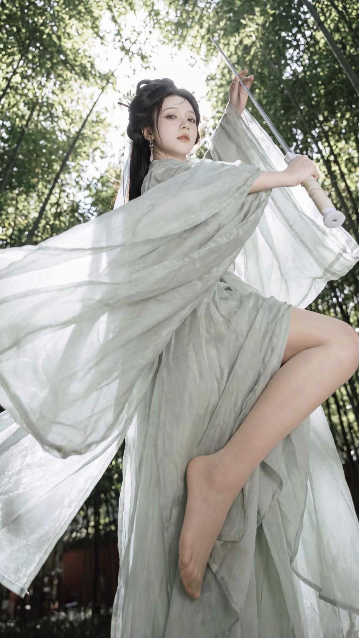 一袭素白汉服，手持长剑，
像是从武侠世界里走出的女侠。
身畔是翠竹摇曳，光影斑驳