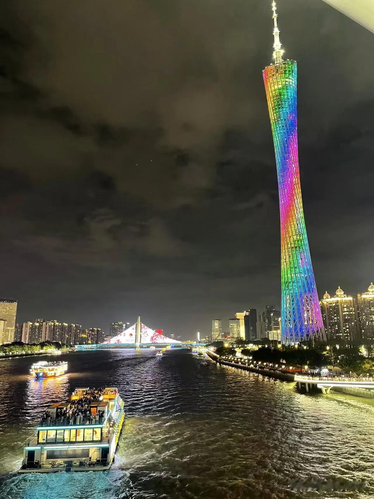 夜幕下，广州塔身披彩衣，如梦幻巨柱直插云霄。珠江波光粼粼，游船载着欢声笑语穿梭，