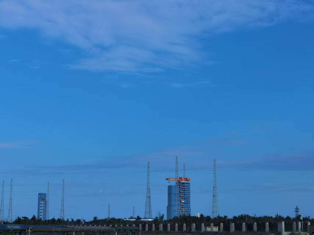 澄澈如洗的蓝天，像一块巨大的蓝宝石铺在头顶，几缕云丝轻描淡写地掠过。发射塔架在海