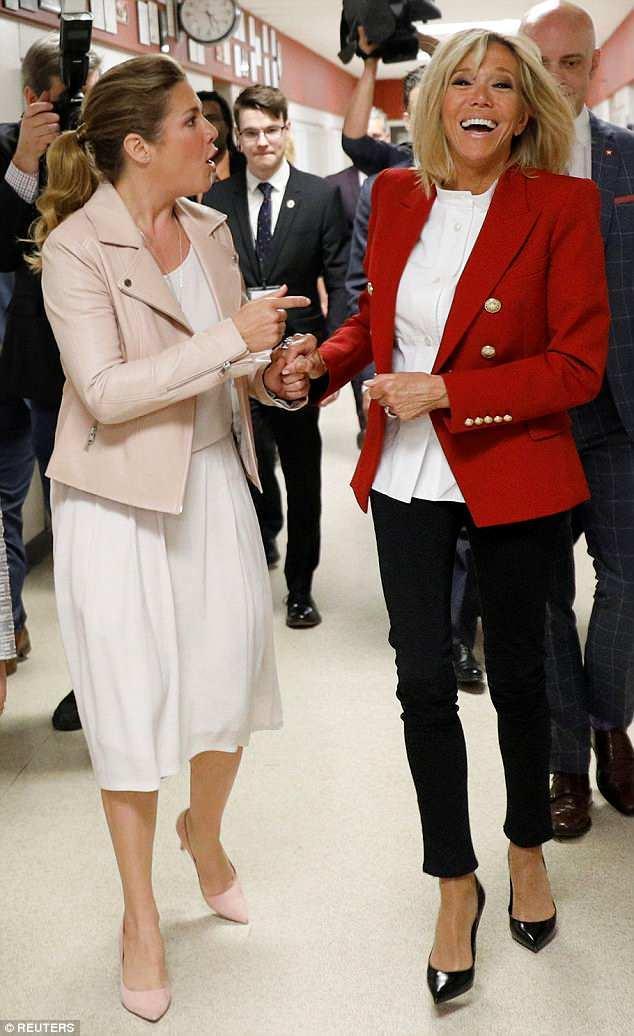 马克龙的妻子一身红衣笑得很灿烂，这个女人内核强大，马克龙在她身旁一副开心的模样。