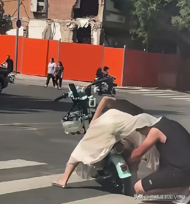 一名女子的裙子缠进了电瓶车，一名路过的大哥热心的帮他把裙子一点点的慢慢抽出来。第