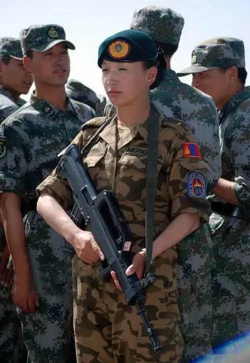 一个蒙古国女兵端着冲锋枪，被摄像师抓拍到，面对摄像头，她眯缝着眼，投来了蔑视的神