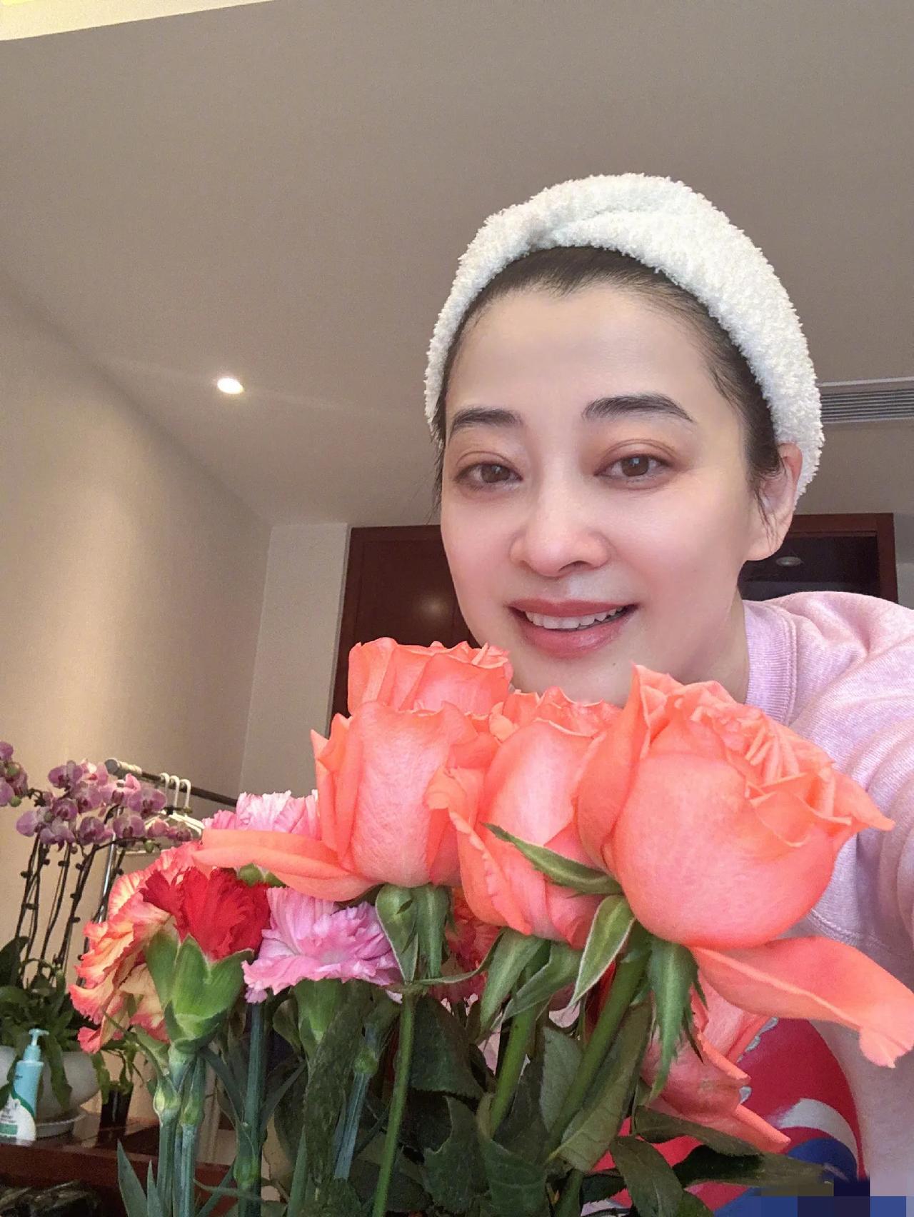 梅婷晒素颜居家照，祝女生节快乐！照片中，梅婷身穿粉色卫衣，头戴白色发带，手捧鲜花