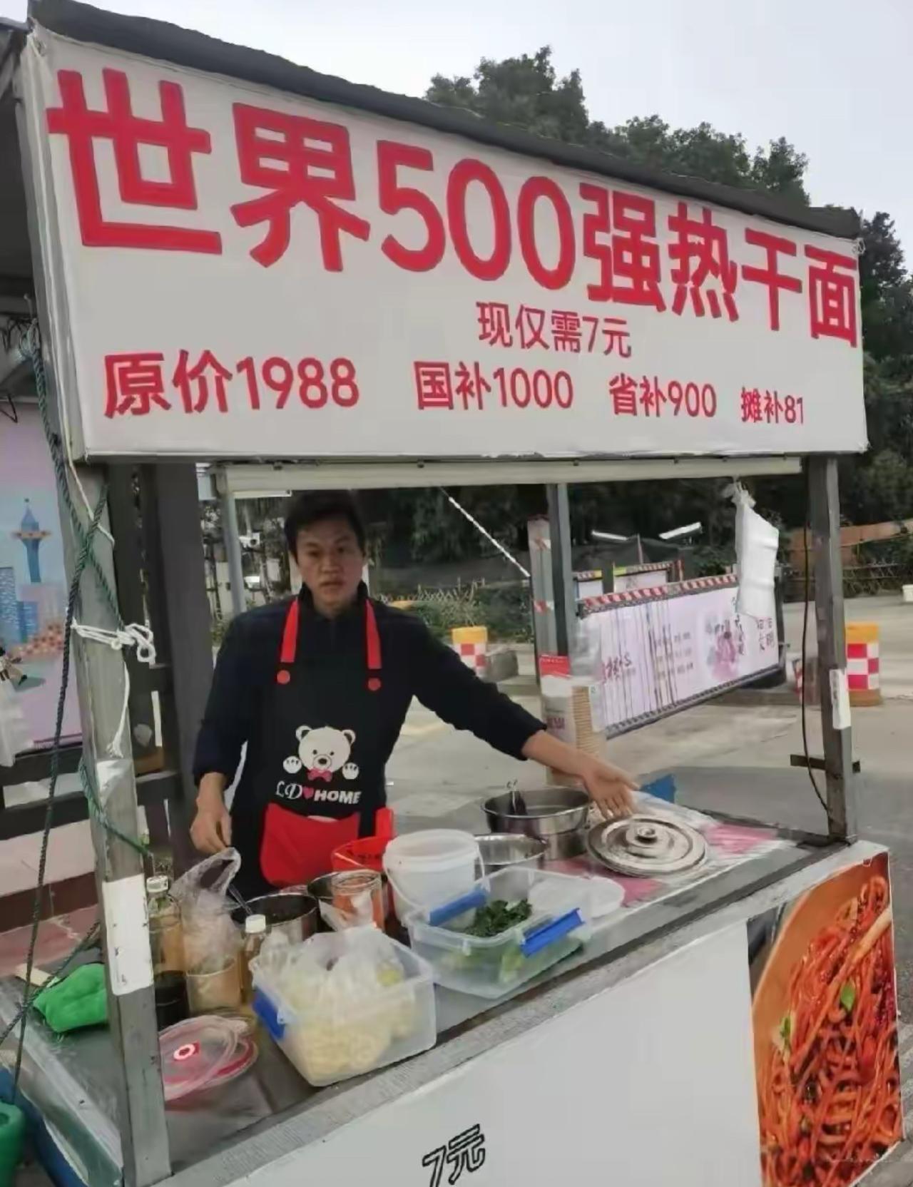 路边一个不起眼的小吃摊，招牌直接打出世界500强热干面的名头，噱头拉满。

一碗