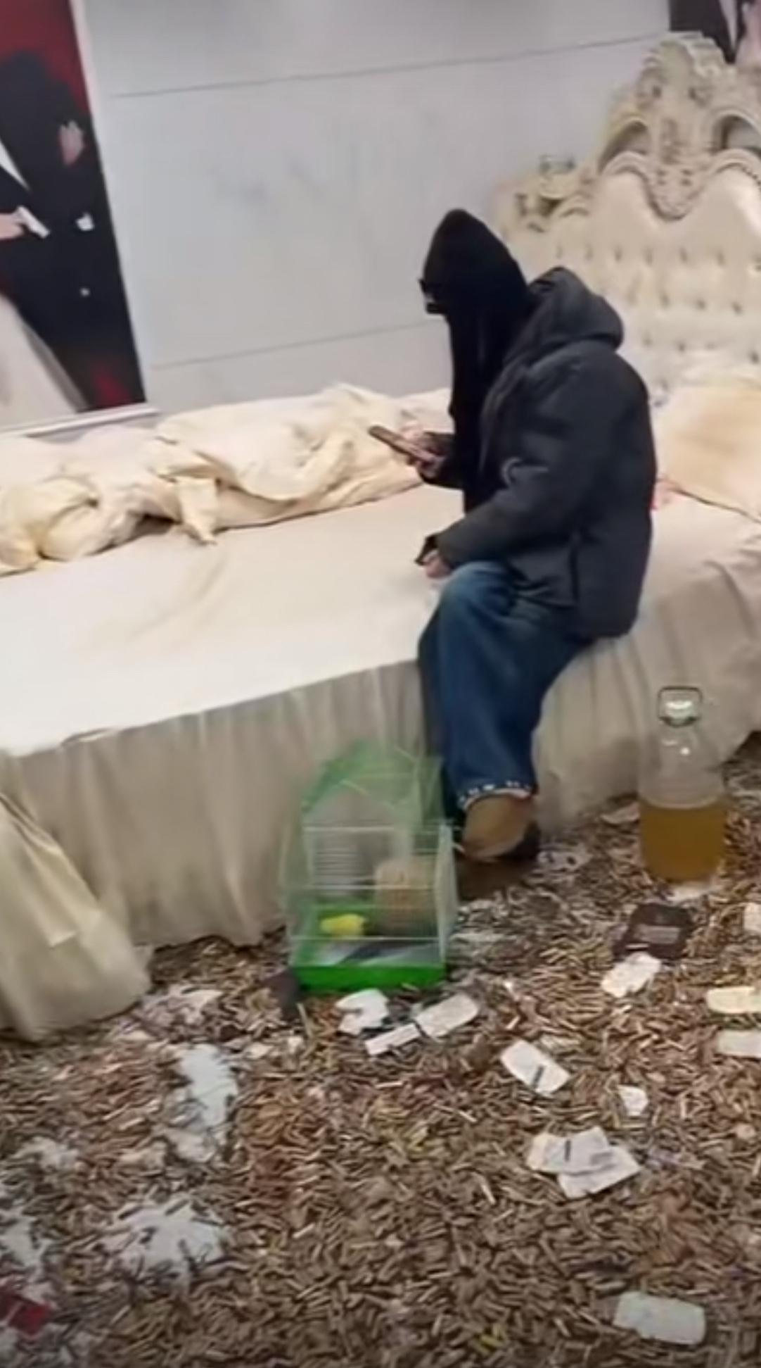 满屋烟头铺满地面，床铺凌乱不堪，这人裹着头套窝在床边只顾刷手机，角落还摆着一缸不