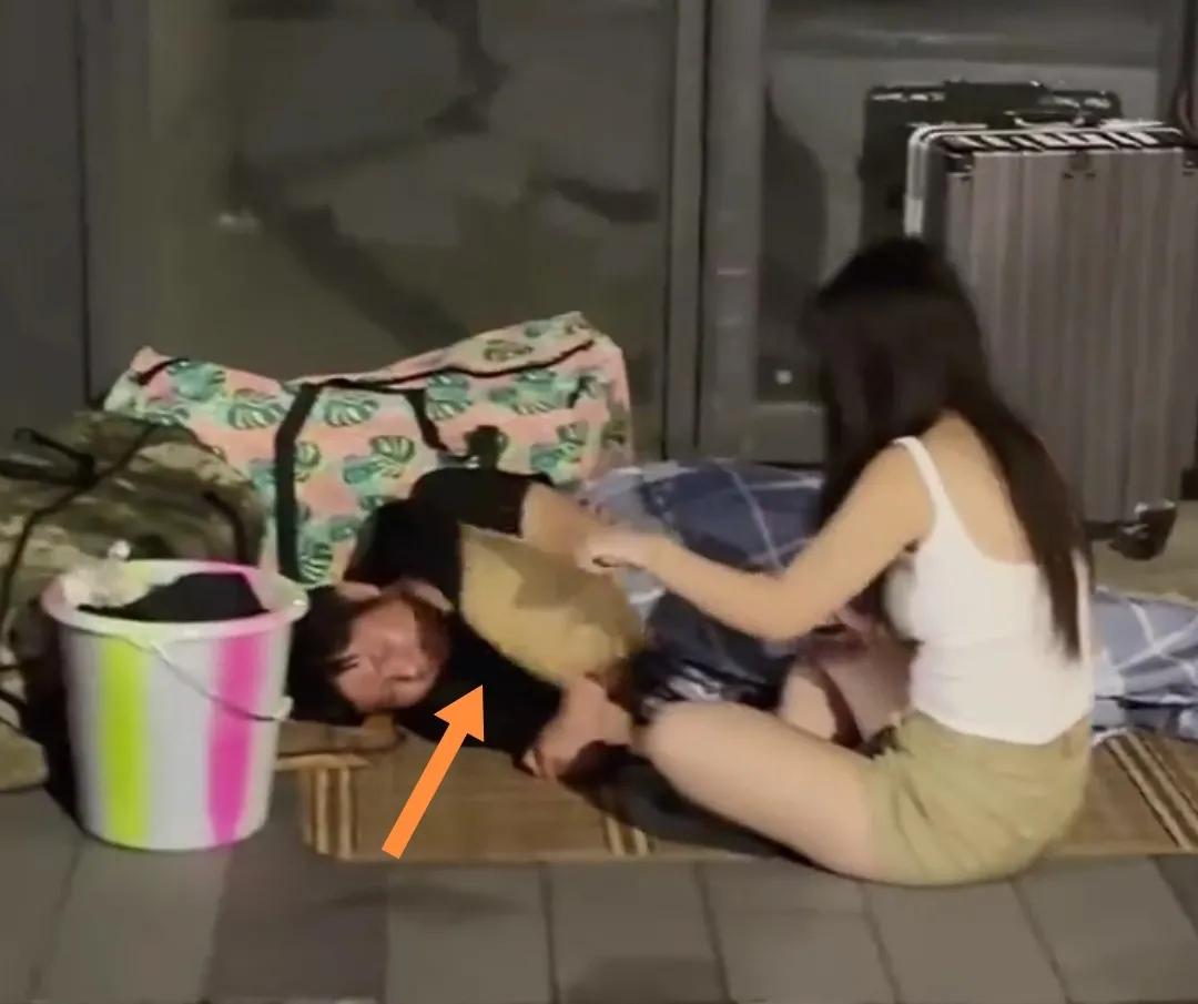 深夜车站门口地上一女子手摇扇子为丈夫扇风赶蚊虫。
