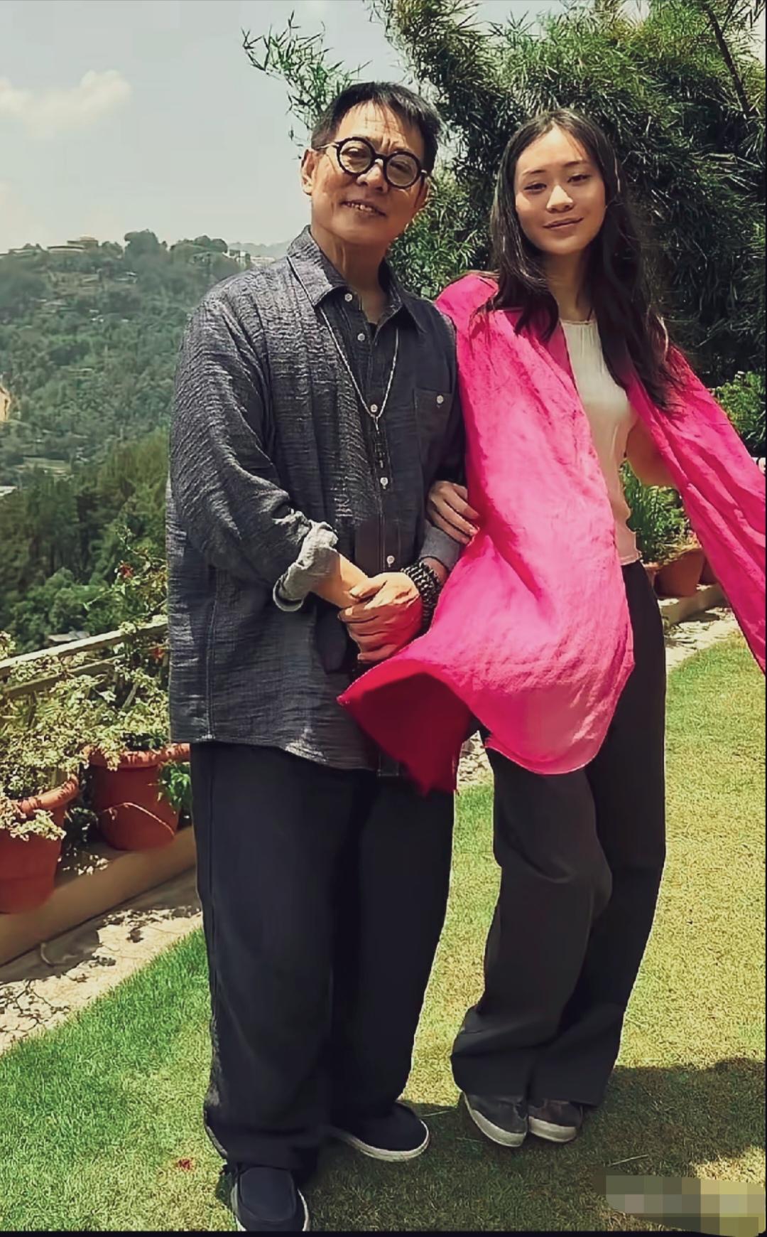 李连杰与小女儿在尼泊尔的户外合影，李连杰戴着黑框眼镜，双手交叠在身前，腕间佩戴佛