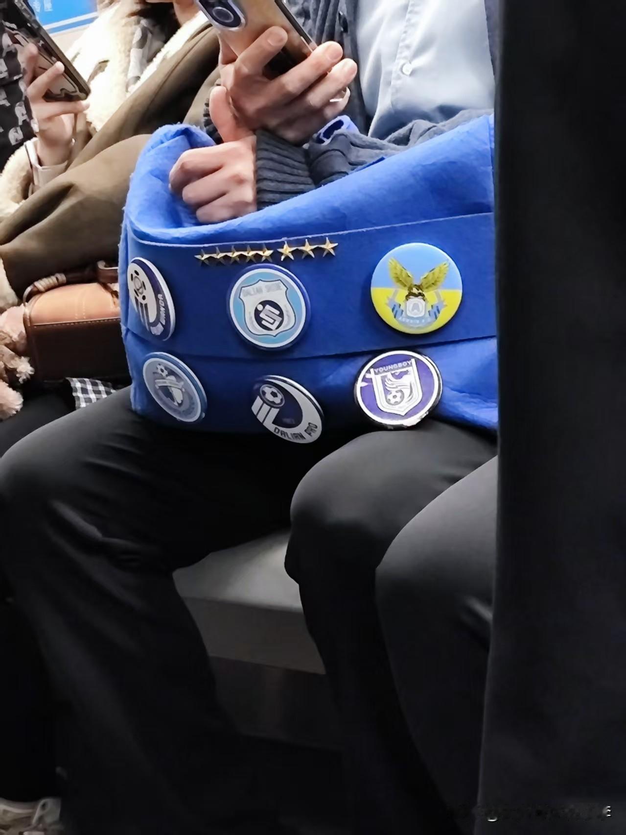 下班在地铁上看到一大连球迷拿的包，蓝色的包上面有八颗星，八颗星的下面是大连万达、