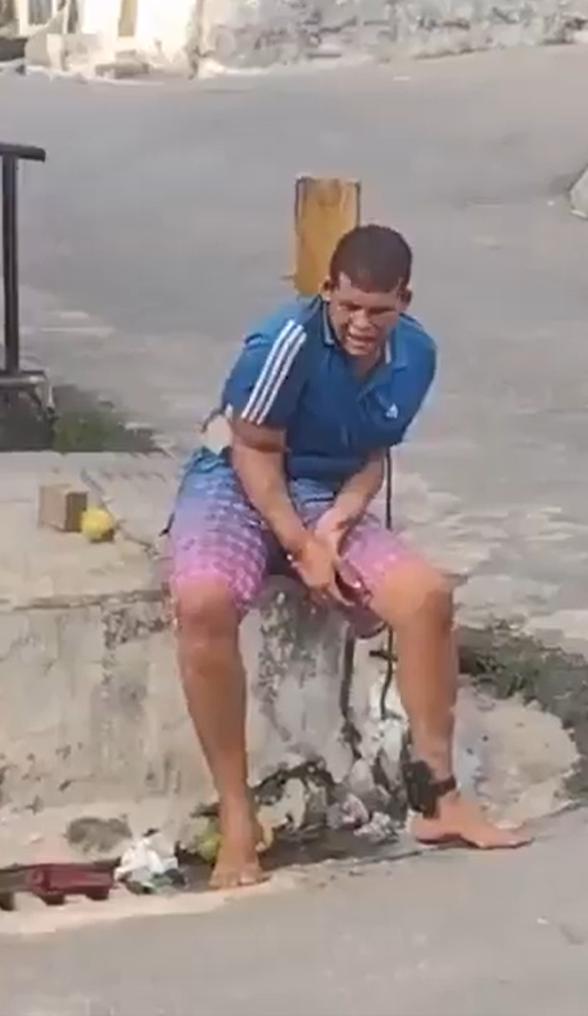 一名赤脚男子戴着电子脚镣，神情沮丧地坐在巴西某街头，显然是被束缚着。他声称自己试