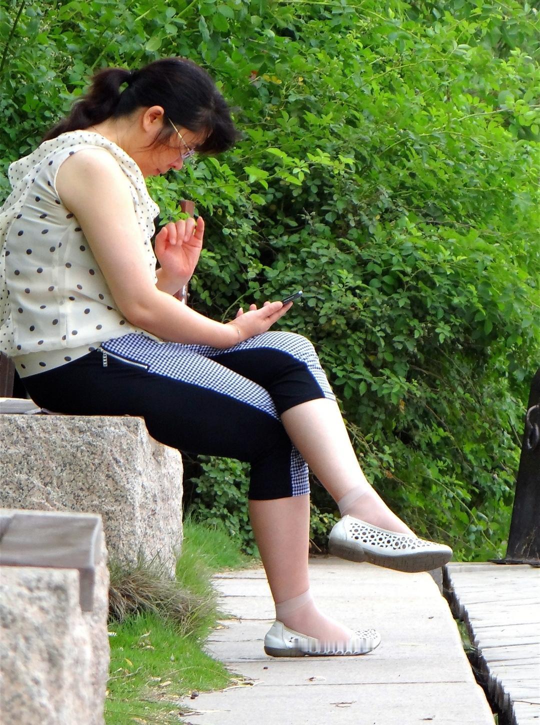 2012年公园的旧相机照片里，石凳置于绿荫之间，一位女士正全身心沉浸在手机里。那