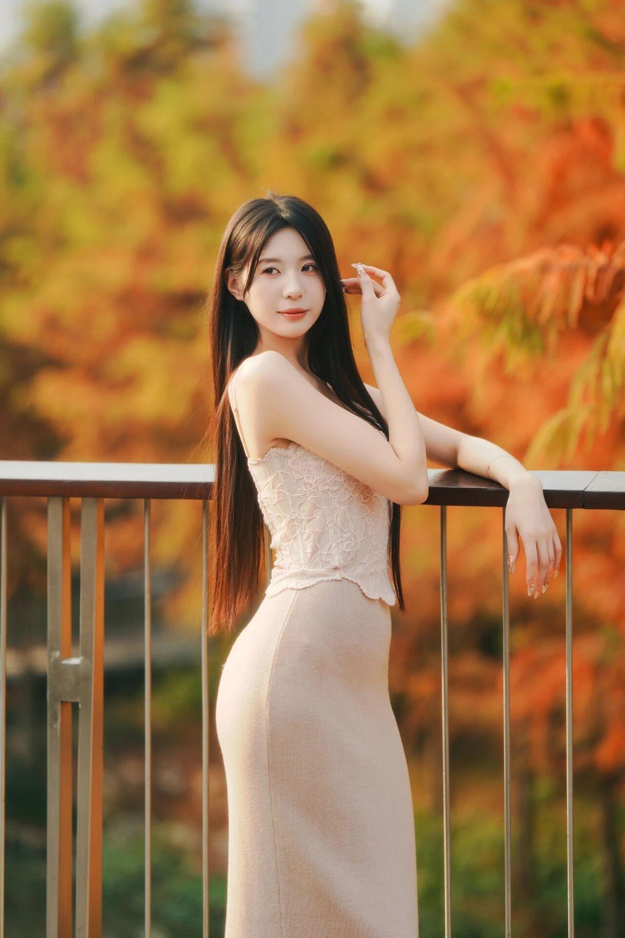 这组照片中的女子宛如秋日里的温柔诗篇，气质清冷又迷人。
她身着浅杏色蕾丝吊带长裙