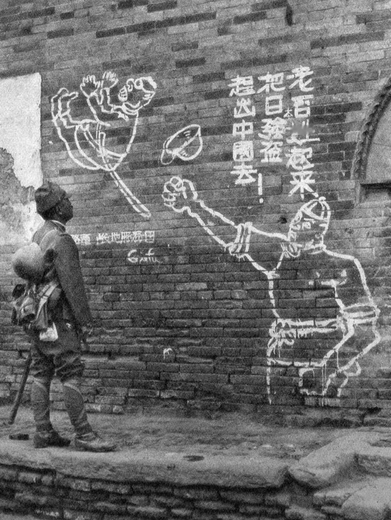 1938年2月，一名侵华日军士兵正在观看某中国城市街头的抗日标语涂鸦。 