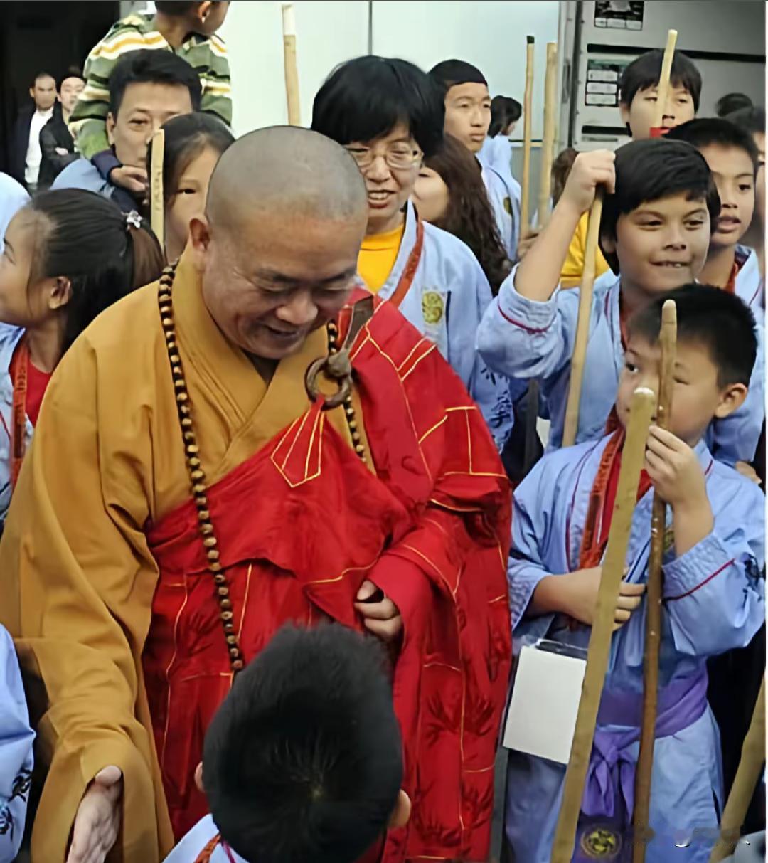 释永信身着红黄色僧衣，佩戴长串佛珠，俯身伸手和面前的学员互动。看得出来他非常关心