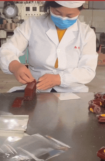 这位大姐帽子、口罩、工作服一应俱全，看着挺规范，结果上手包装就露馅。山楂卷直接徒