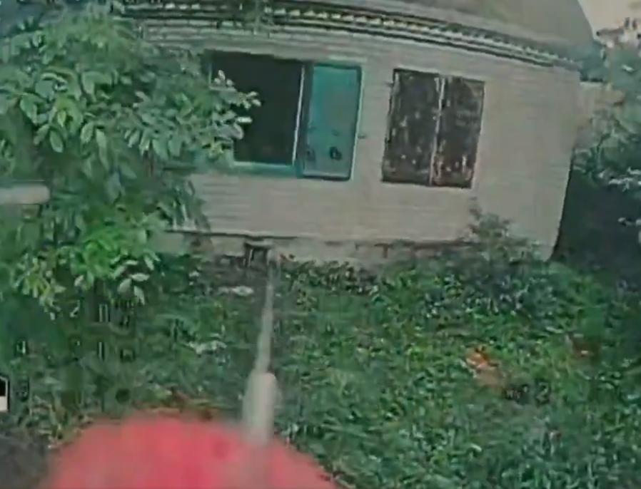 俄罗斯 FPV 无人机显示：在被绿色植物包围的受损建筑物的外部一无人机接近并通过