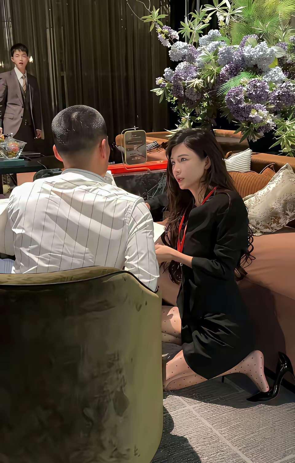 女士敬业的精神着实令人钦佩。一位男士惬意地倚靠在沙发上，旁边有位少女以半跪的姿势