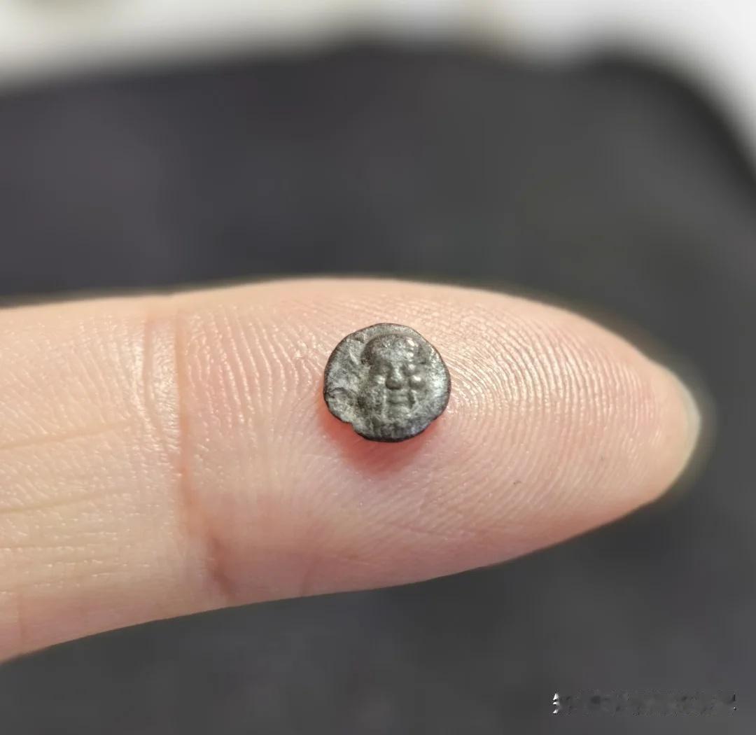 手指肚上的圆形金属，是古希腊的一种银币—奥波，6个奥波相当于1德拉克马，很小，还