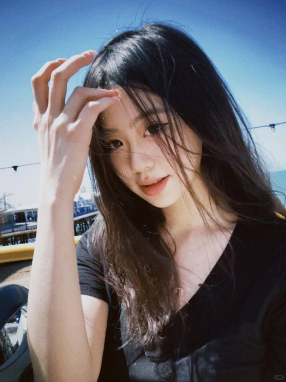 阳光明媚的一天，少女在海边轻抚发丝，享受美好时光。分享美少女倩影 海边 海边活力