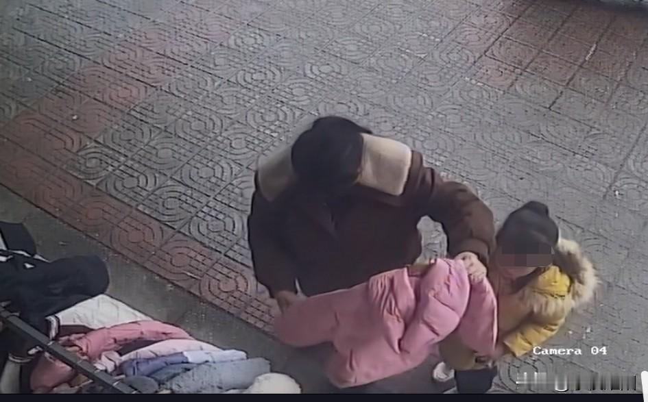 母亲当着孩子的面偷衣服。图中监控画面显示，在一街道上，一名着棕色衣服的女子带着一