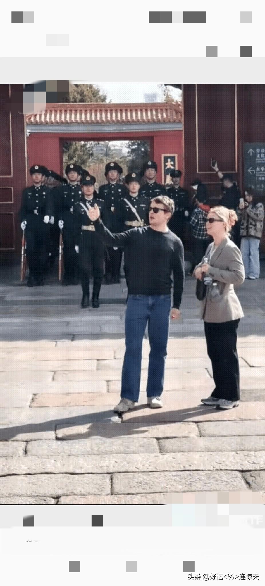 两名外国游客站在故宫前观赏风景，在他们身后的，国旗护卫队的小伙子们，迈着整齐划一