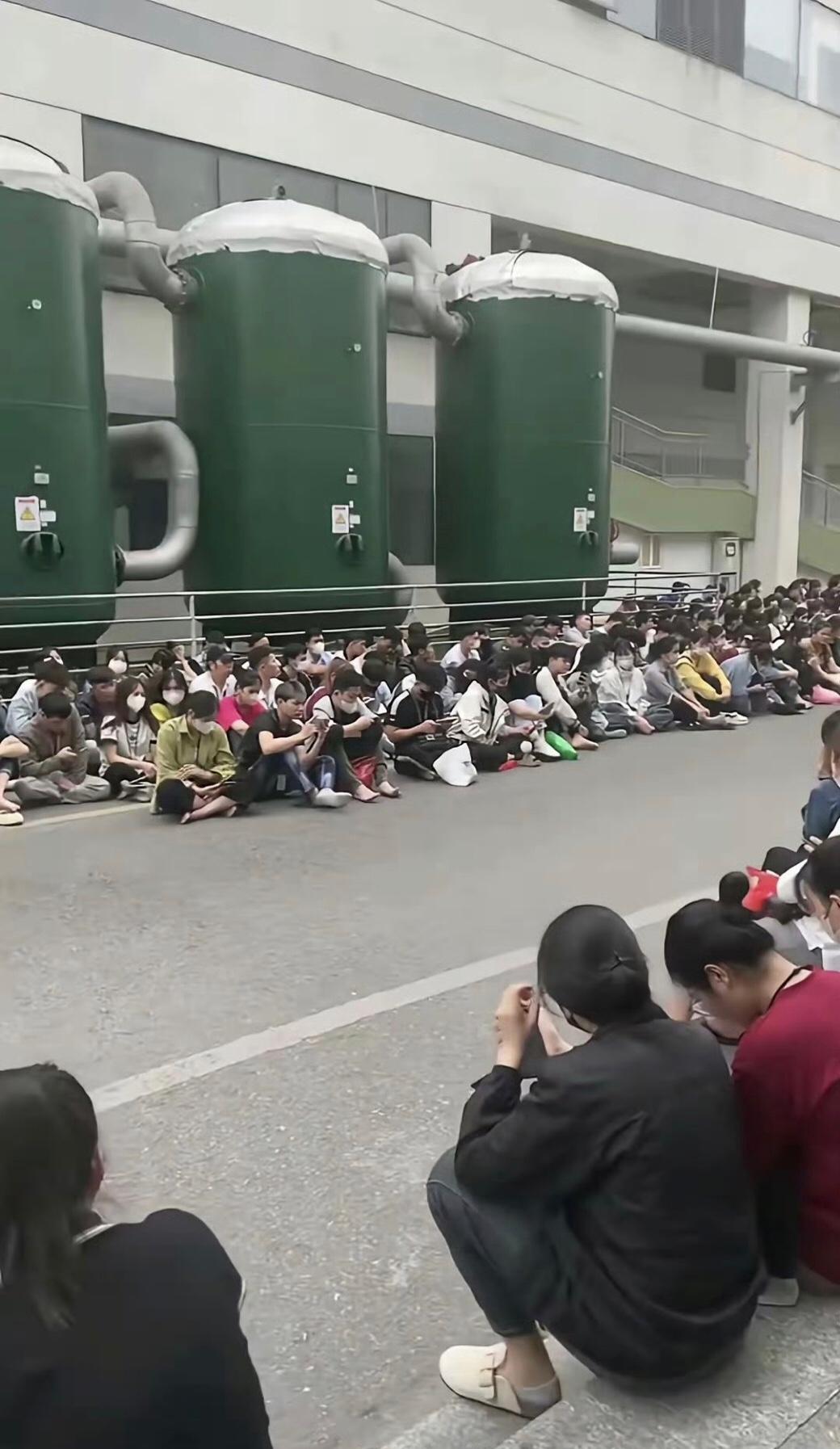 越南的工厂又停电了，年轻的工人们只能在工厂外一排排坐着等待恢复通电，好继续打工挣