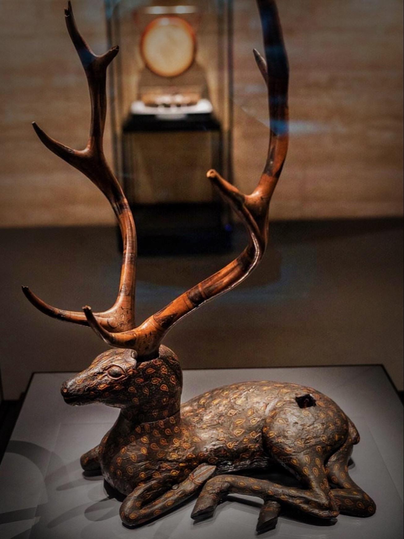 东周· 彩漆木雕梅花鹿。犬吠水声中，桃花带露浓
树深时见鹿，溪午不闻钟
野竹分青霭，飞泉挂碧峰
无人知所去，愁倚两三松
——唐·李白《访戴天山道士不遇》 
这件梅花鹿身长45厘米，身高27厘米，鹿角高50厘米，曾侯乙墓出土，湖北省博物馆藏 
身体用整木雕成，头上插着真鹿角，头部可以自由转动
眼眶、口唇、鼻孔用鲜红的浓漆点涂
鹿的四肢蜷曲，昂首凝望，神态自若，造型逼真 
在先秦时代，古人认为梅花鹿是下凡灵物，放在墓中可以通灵，引灵升天 
出土时与琴、瑟相伴，后腿有一方孔，推测孔内曾经插有一面小木鼓