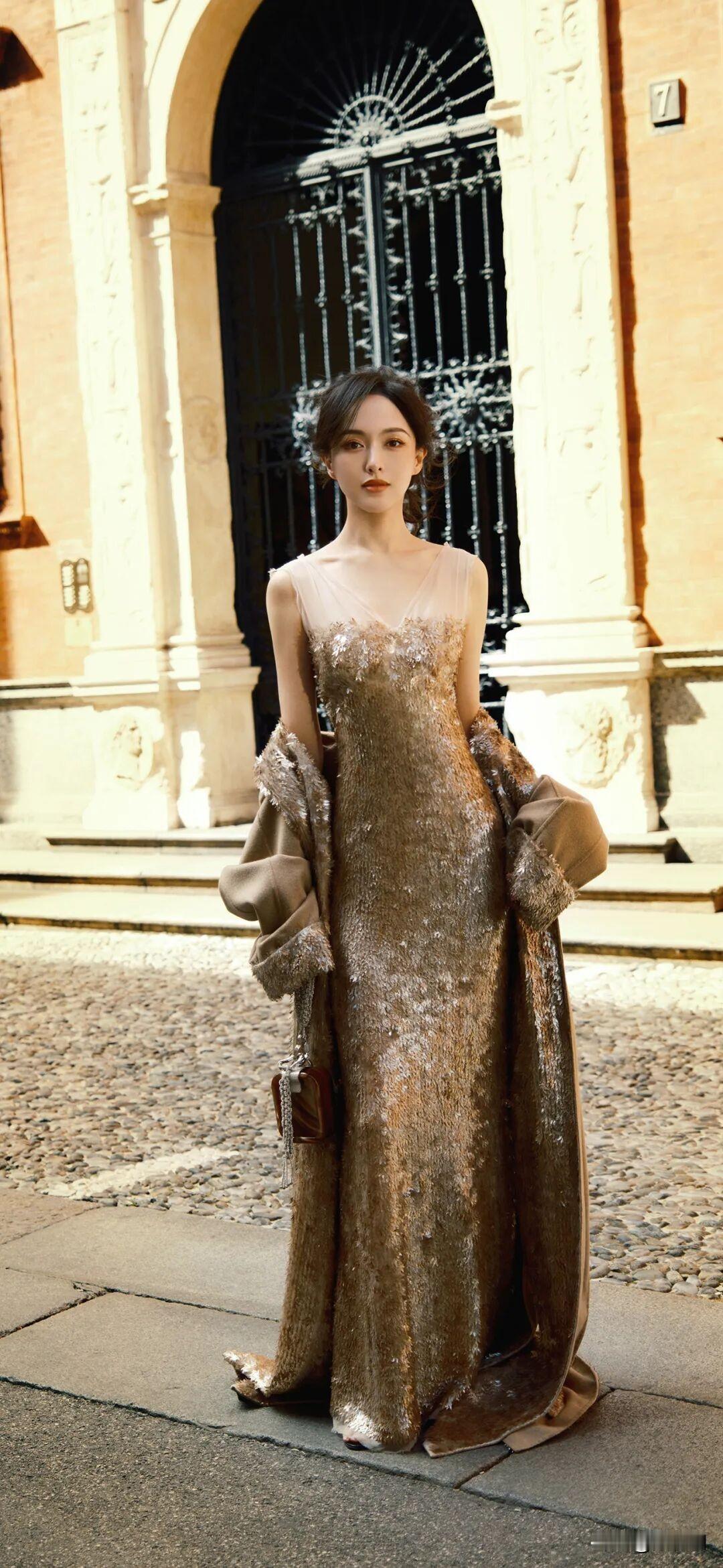 金缕裁裙映暖阳，
玉颜凝睇立宫墙。
风拂鬓影添清绝，
一刹风华动米兰。