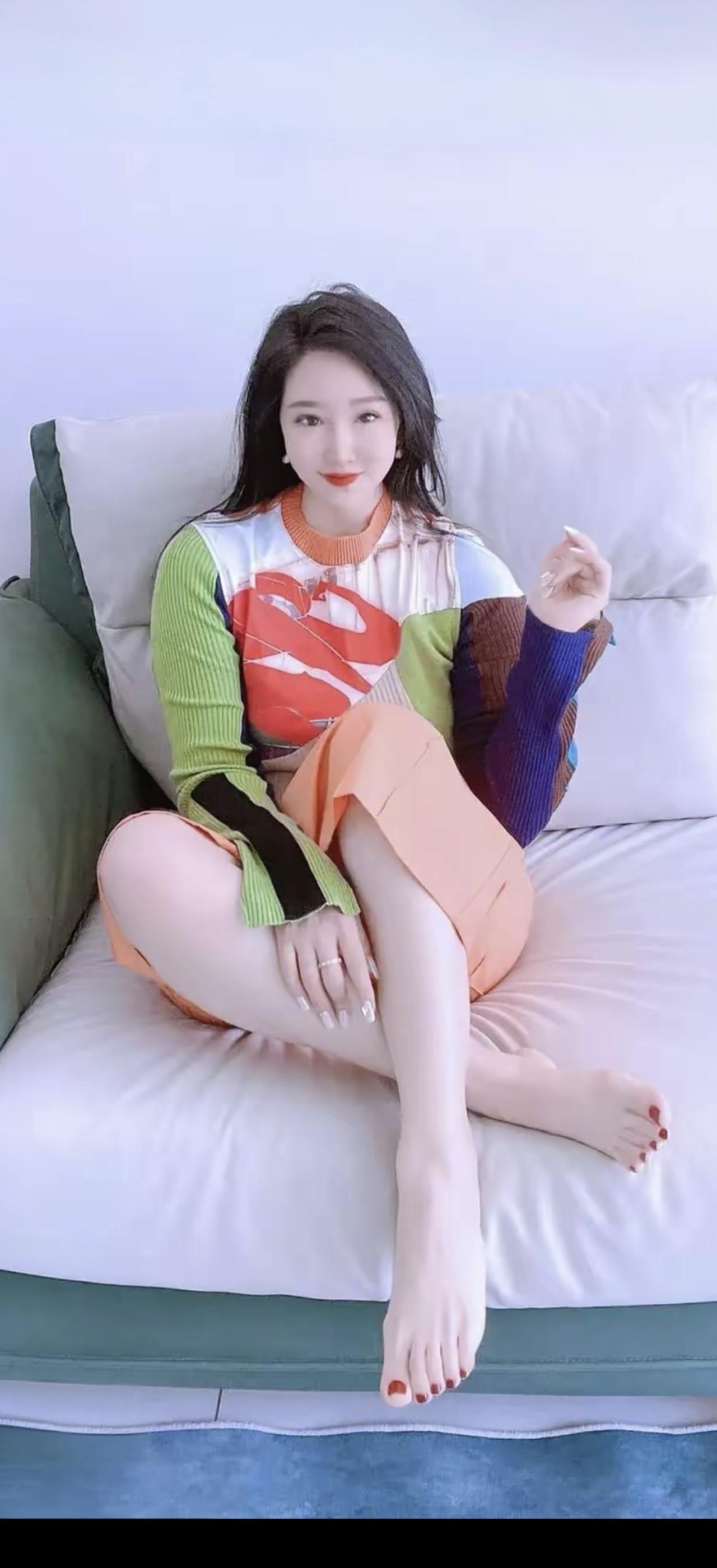 她坐在沙发上，穿着彩色毛衣和裙子。