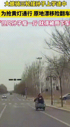 路口黄灯亮起，一位大娘骑着三轮车，车上还载着孙子。
大娘没留意信号灯，直接就往前