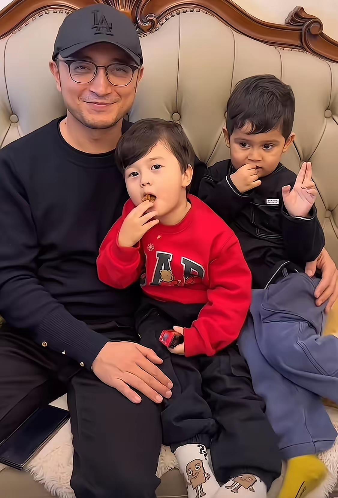 奶爸带娃的温馨时刻，两个小宝贝一个认真炫零食，一个乖巧比耶，画面里全是藏不住的幸