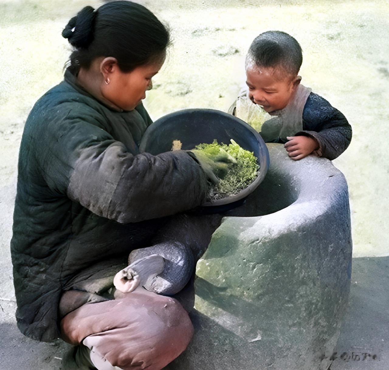 河南洛阳，大饥荒的寒冬里，一位穿着棉袄棉裤的母亲用陶盆盛着树皮与草根。旁边孩子直