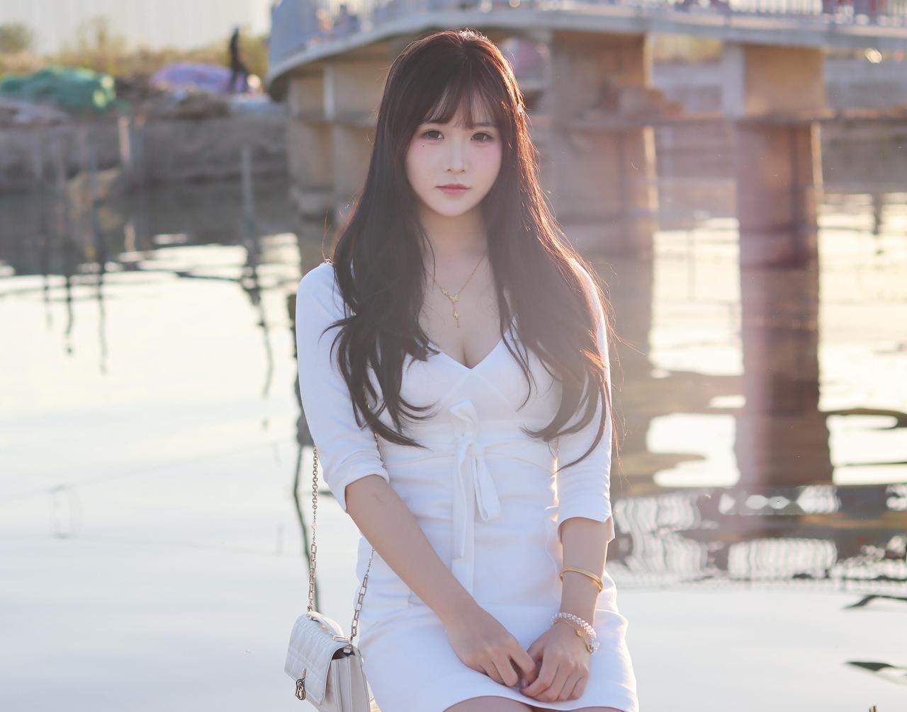 落日把金箔揉碎，铺在粼粼的水面
她坐在石球上的模样，像一截被温柔裹住的时光
白裙