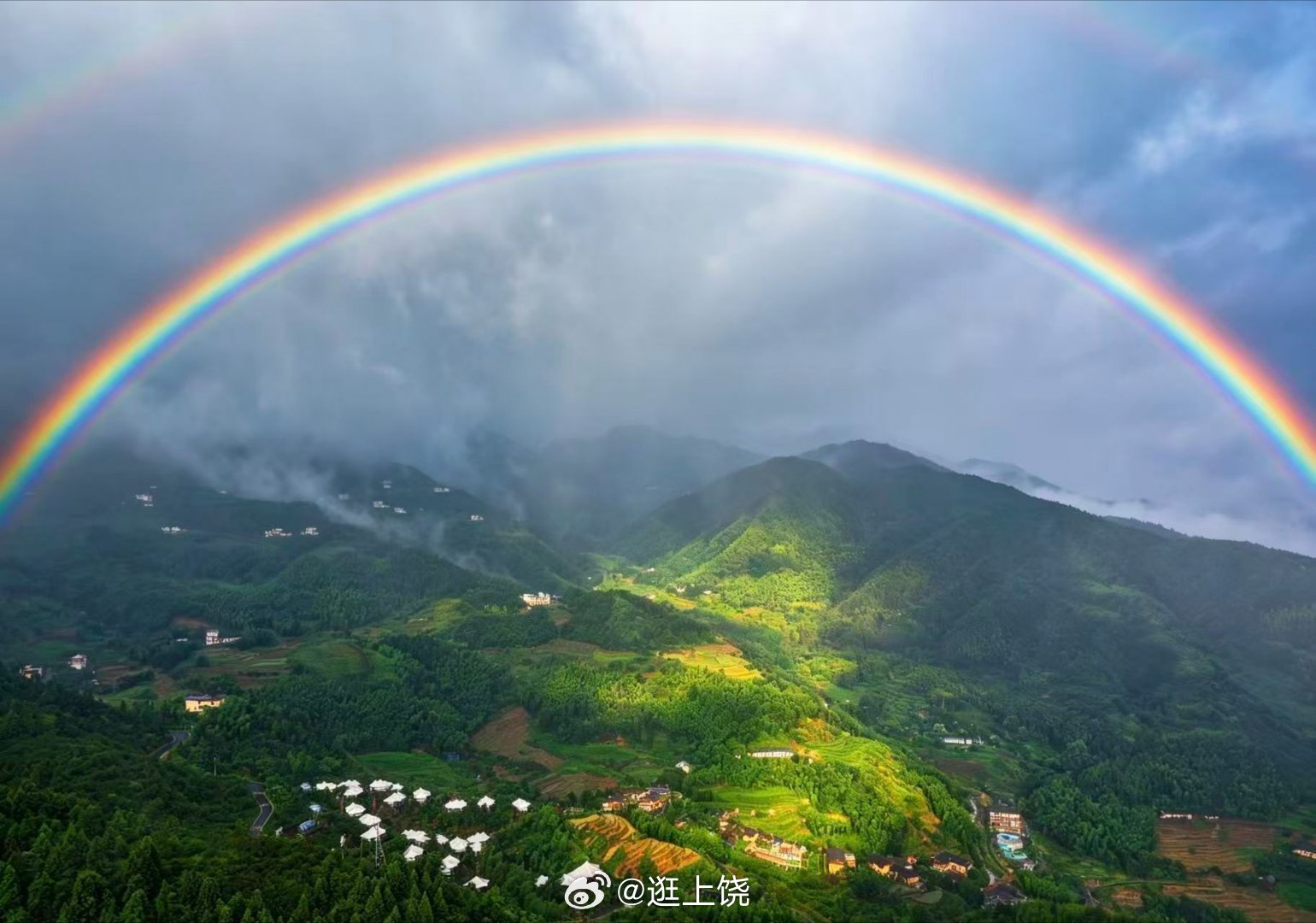 山雨初收，云雾缠绕层叠青山，一道完整的彩虹横跨天际，温柔笼罩山谷间的村落与梯田。