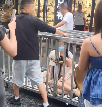 一段女子被锁金属铁笼沿街推行的短视频此前在全网刷屏，画面里笼中还放有黑狗，旁边立