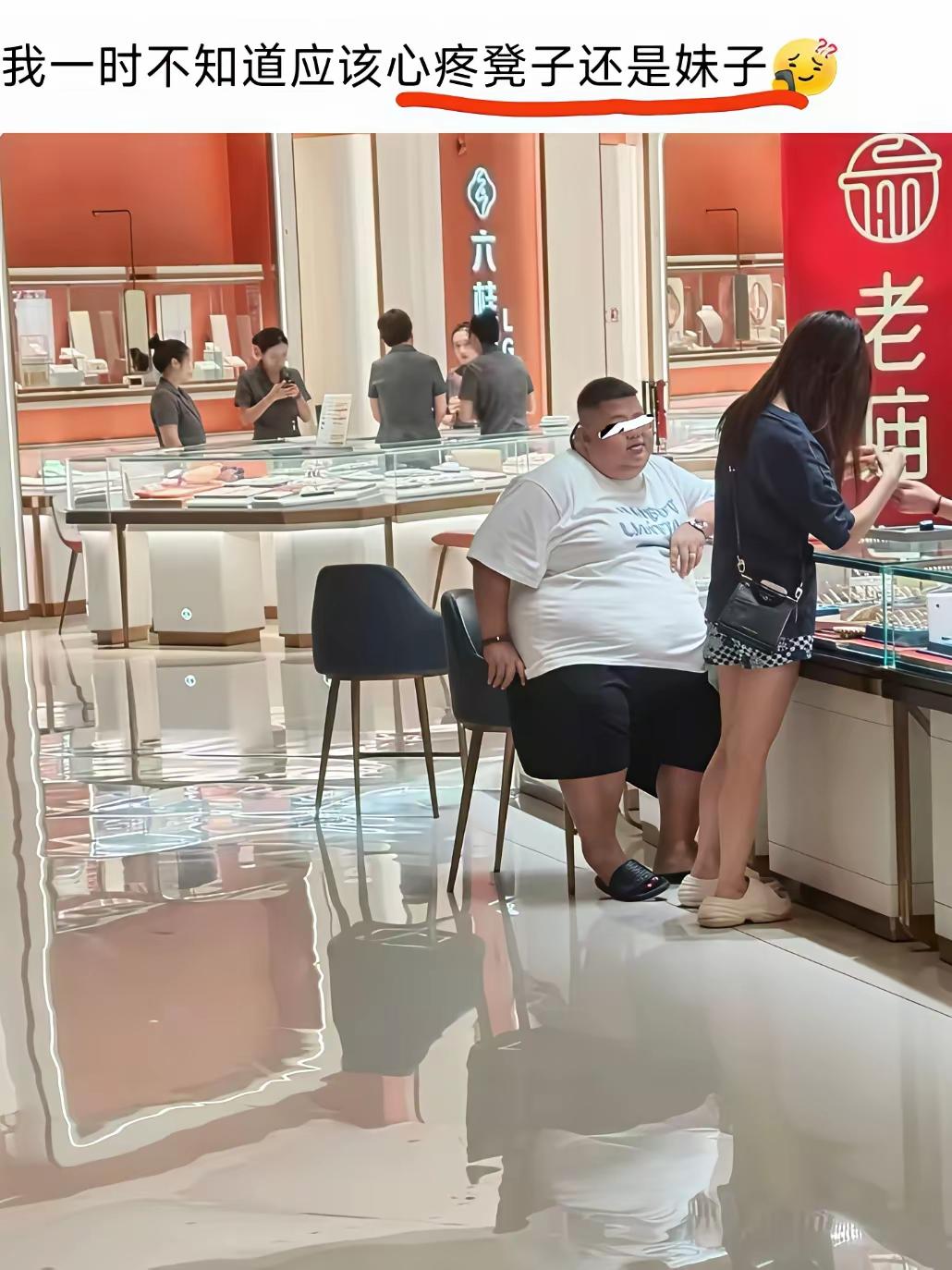 金店。
白衣胖男陪娇小黑衣女朋友买首饰，女朋友站在柜台前挑选首饰，白衣胖男坐在凳