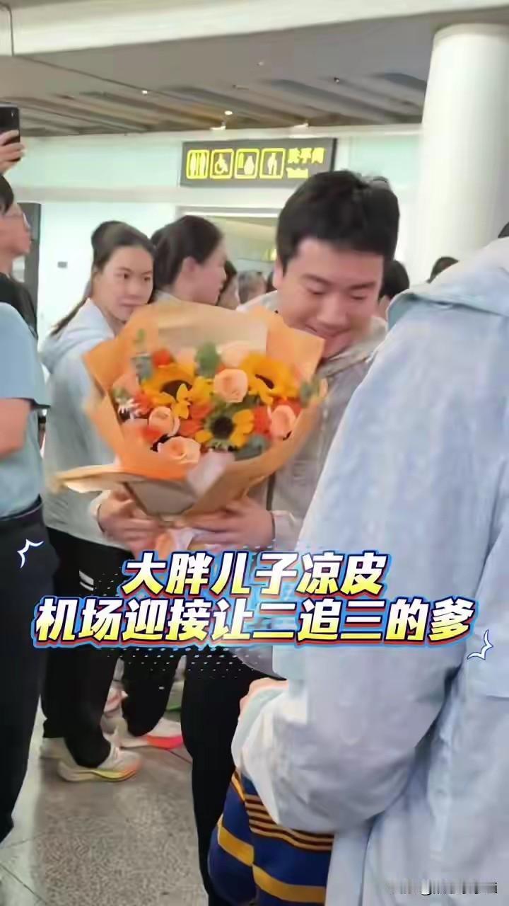粱靖崑回到北京，看到老婆带着两个孩子来接机，手捧着鲜花手，露出了幸福的笑容，开心